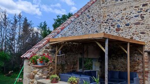 Edificio de piedra con un patio cubierto, mobiliario exterior y plantas en macetas.