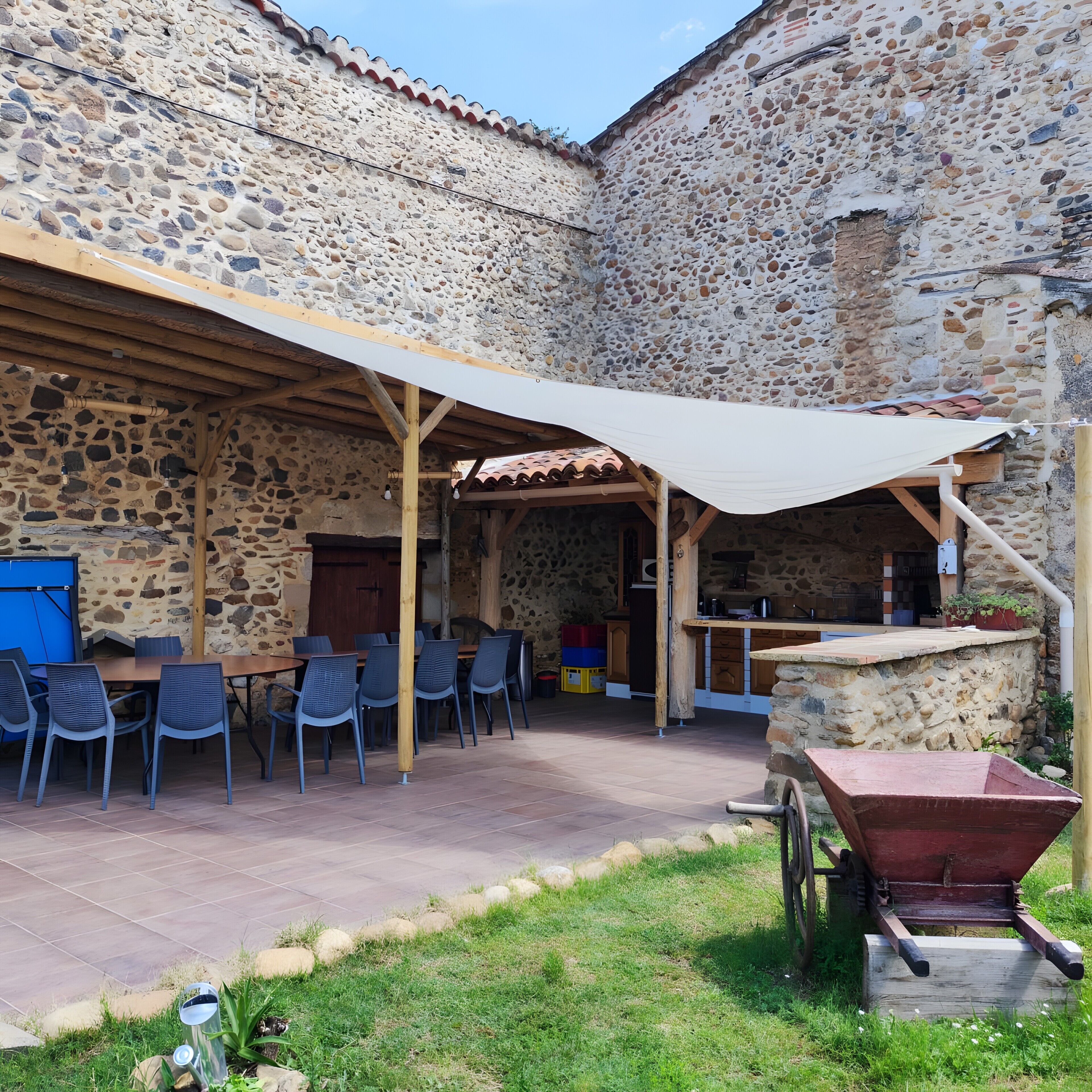 A stone building with a covered patio, outdoor seating, and a wheelbarrow.