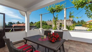 Une terrasse extérieure avec une table et des chaises, un pot de fleurs et une vue sur des bâtiments et des arbres.