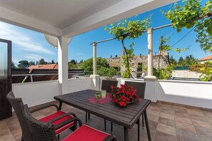 An outdoor patio with a table and chairs, a potted plant, and a view of buildings and trees. - Above the Blue: 2BR Tranquil Horizon Pool&Terrace (Bosanka)