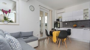 Un salon moderne avec un canapé gris, un coin repas avec une nappe jaune et des meubles de cuisine blancs.