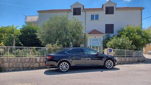 Une voiture noire est garée devant un immeuble doté d’un toit recouvert de tuiles et de nombreuses fenêtres.