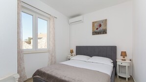 Une chambre à coucher comprenant un lit, deux tables de chevet, une fenêtre avec des rideaux, un appareil de climatisation et un tableau accroché au mur.