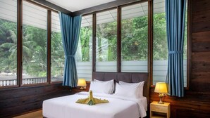 A large bed with white linens, a wooden headboard, and a nightstand with a lamp. - Rawa Island Resort (Mersing)
