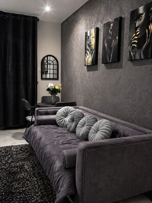 A modern living room with a grey sofa, black curtains, and three framed artworks on the wall. - Wonderland Art House 2BR Loft Melville Walk to 7th With Secure Parking (Johannesburg)