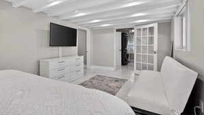 Een slaapkamer met een bed, een televisie, een dressoir en een deur naar een wasserette.