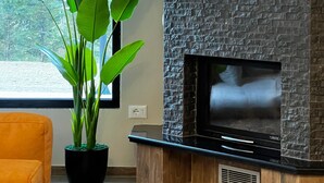 Un salon moderne avec une cheminée, une grande plante en pot et une fenêtre donnant sur un paysage verdoyant.