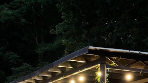 Un espace extérieur aménagé avec des sièges couverts, des guirlandes lumineuses, des chaises et une structure en forme de pergola.