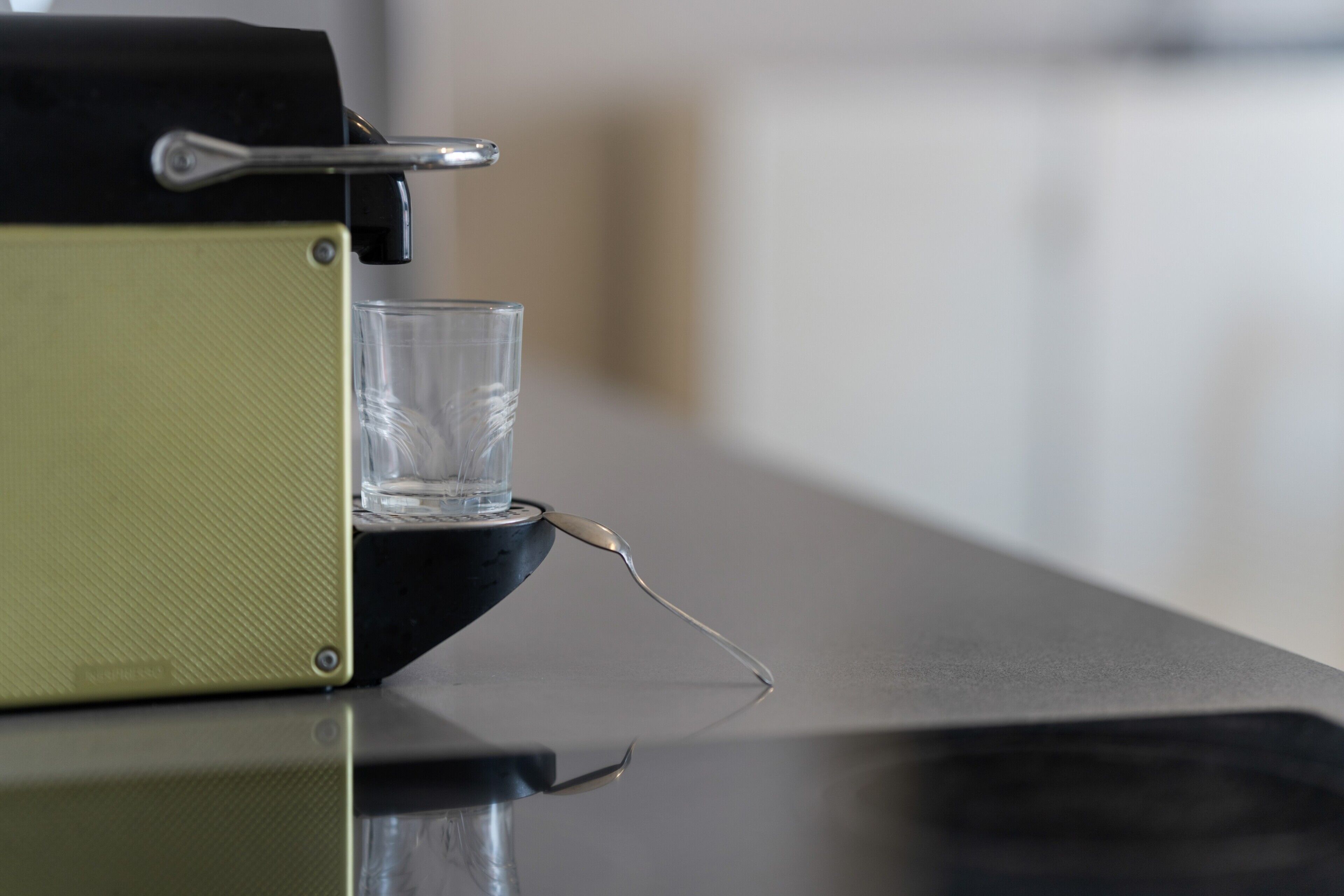 A coffee machine with a glass of water on a reflective surface.