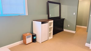 Una habitación pequeña con un refrigerador blanco, un calentador de madera, un aparador negro y un espejo en la pared.
