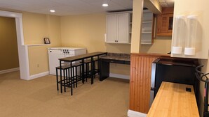 Una cocina compacta con una mesa de madera, taburetes de bar, un refrigerador blanco y un armario de madera.