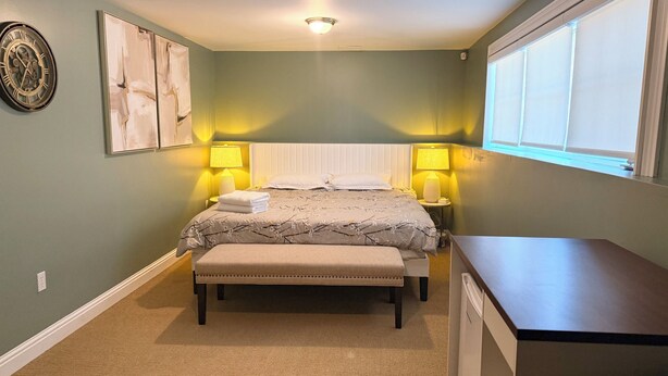 Un dormitorio con cama, lámparas de noche, un banco, un escritorio y una ventana.