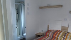 Ein Schlafzimmer mit einem Bett, einem Nachttisch, einem Spiegel und einer Dusche.