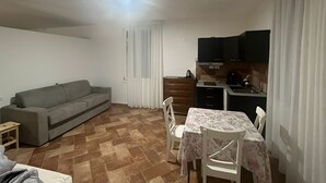 Ett kompakt bostadsutrymme med en soffa, ett matbord, stolar, ett litet kök och en TV.