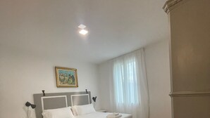 Ett sovrum med en säng, ett nattduksbord, en lampa, en tavla och ett fönster med gardiner.