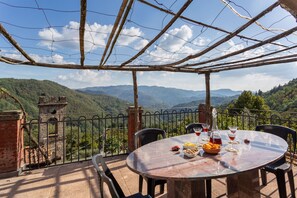 Uma mesa com comida e bebidas, vista para montanhas e uma estrutura de pérgula.