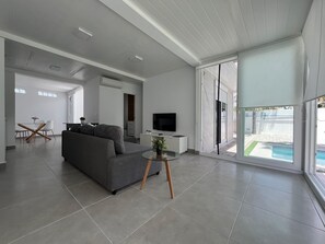 Una sala moderna con un sofá gris, un televisor y una mesa de vidrio con una planta.