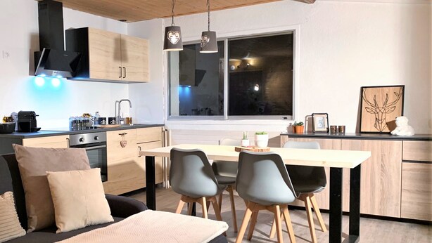 Eine moderne Küche mit Holzausstattung, ein Essbereich mit Tisch und Stühlen sowie eine gemütliche Sitzecke mit Sofa und Kissen.