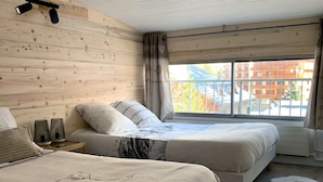 Ein Schlafzimmer mit zwei Betten, Holzboden, einem großen Fenster und Blick auf Gebäude.