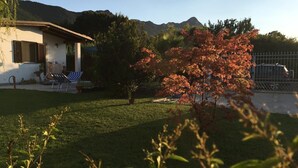 Une maison avec une pelouse, un arbre aux feuilles rouges et des montagnes en arrière-plan.