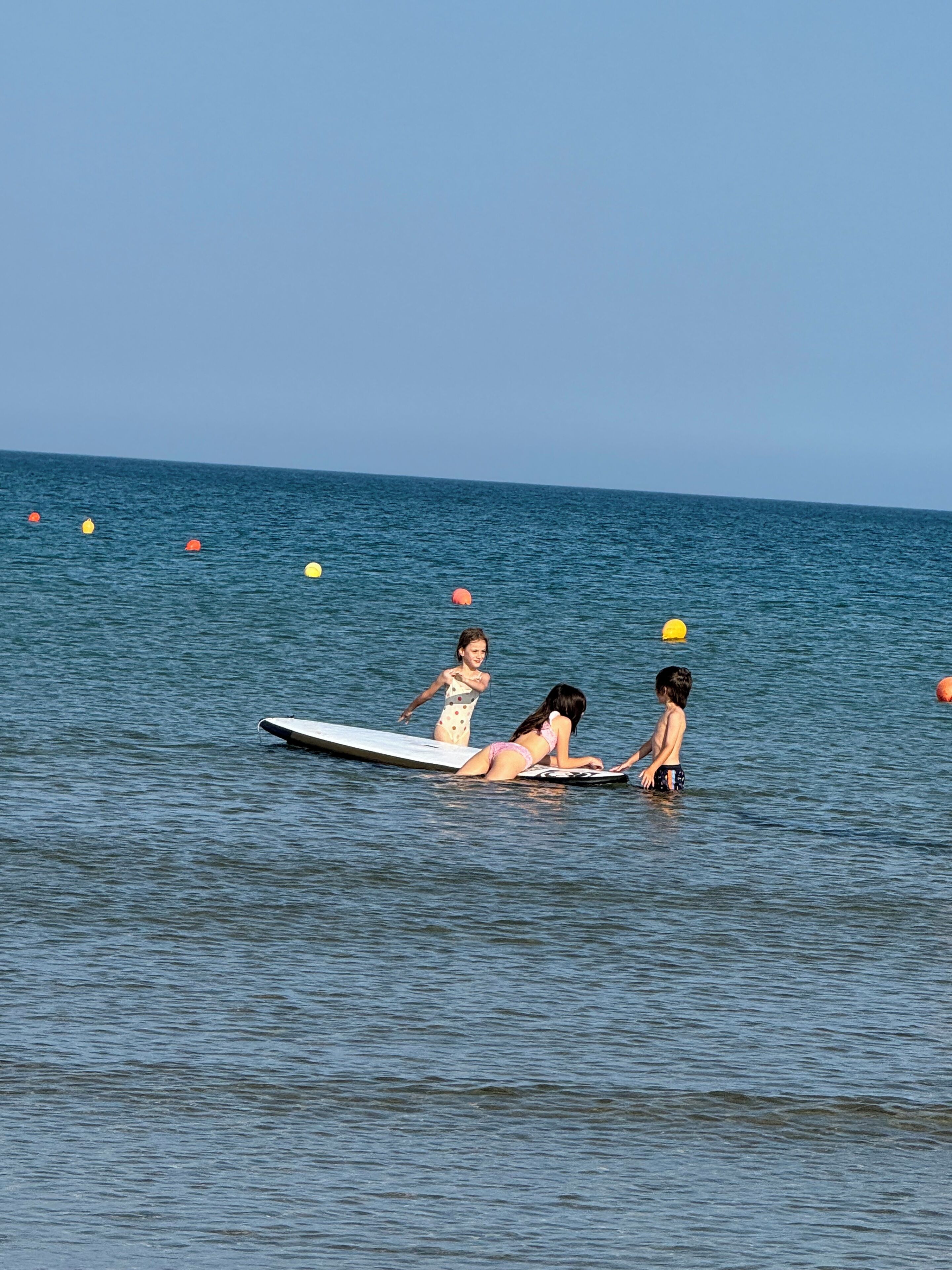Eine Strandansicht mit zwei Personen auf Surfbrettern und Bojen im Wasser.