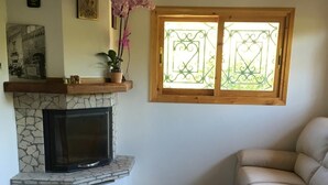 Un salon avec une cheminée en pierre, un canapé, un fauteuil et une fenêtre ornée d’une grille décorative.