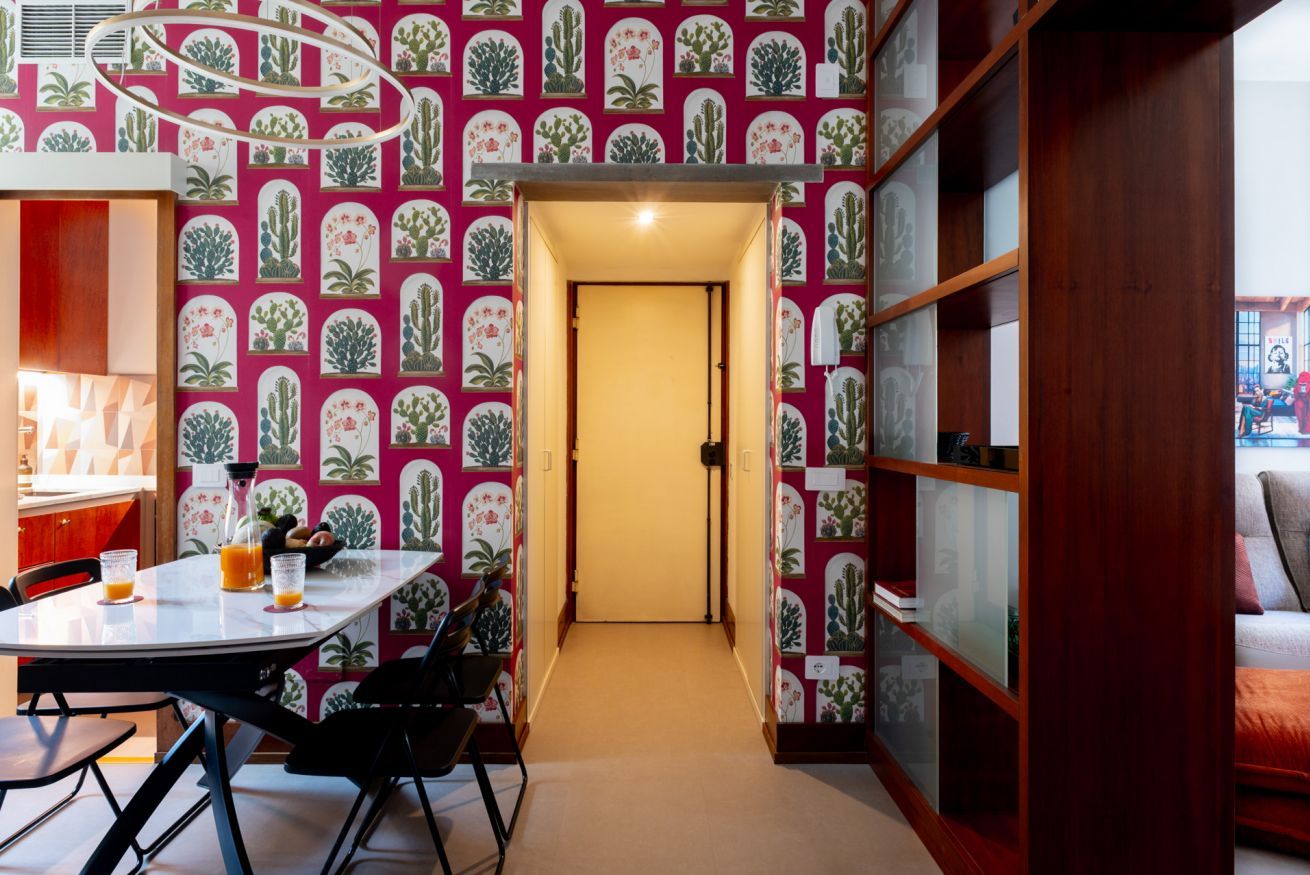 Een kamer met behang met een patroon, een eettafel met stoelen en een boekenkast.