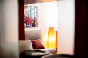 Ett rum med en soffa, en röd kudde, en tavla på väggen och en lampa.