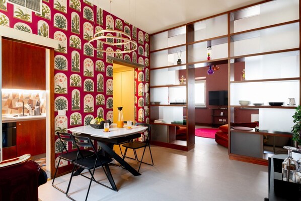 A modern kitchen with a dining area, featuring a patterned wallpaper, a built-in bookshelf, and a red sofa. - Joyful Lungarno Apartment (Florence)