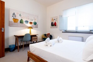 Une chambre d’hôtel avec un lit, un bureau, une chaise, une lampe et des œuvres d’art accrochées aux murs.