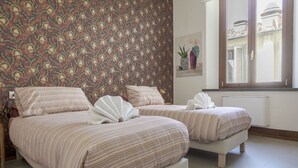 A hotel room with two beds, a patterned wallpaper, a window with a view, and a radiator. - Joyful Lungarno Apartment (Florence)