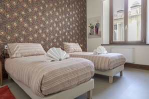 A hotel room with two beds, a patterned wallpaper, a window with a view, and a radiator. - Joyful Lungarno Apartment (Florence)