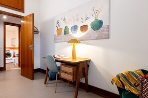 Una habitación con un escritorio de madera, una silla, una lámpara y una obra de arte en la pared.