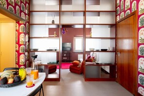 A room with a dining table, chairs, a fruit basket, and a television in the background. - Joyful Lungarno Apartment (Florence)