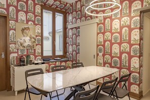 A dining area with a marble table, four chairs, a decorative wall with plant patterns, a window, and a ceiling light fixture. - Joyful Lungarno Apartment (Florence)