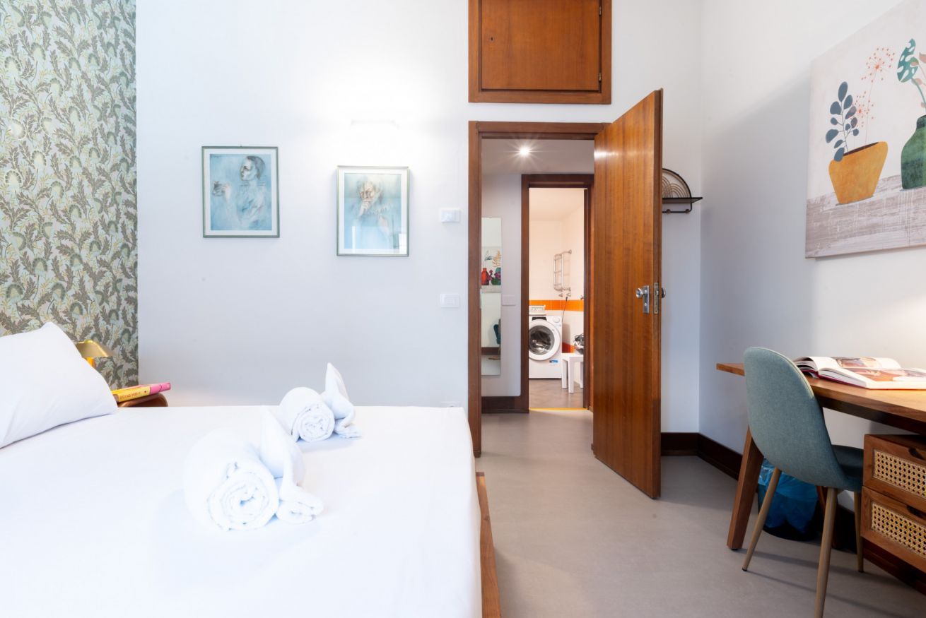 Une chambre d’hôtel avec un lit, un bureau et une chaise. Une porte donne accès à une buanderie.
