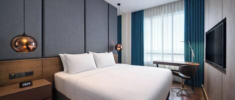 Una habitación de hotel moderna con una cama grande, controles junto a la cama, un escritorio con una silla, un televisor y una ventana con cortinas.