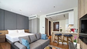 A modern hotel room with a bed, sofa, kitchen area, and a dining table.