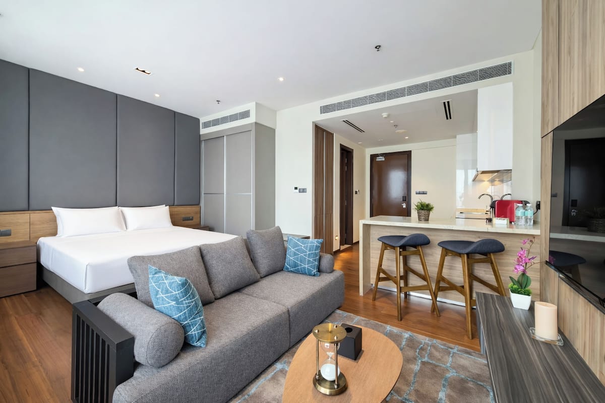 Ein modernes Hotelzimmer mit Bett, Sofa, Küchenzeile und Esstisch.
