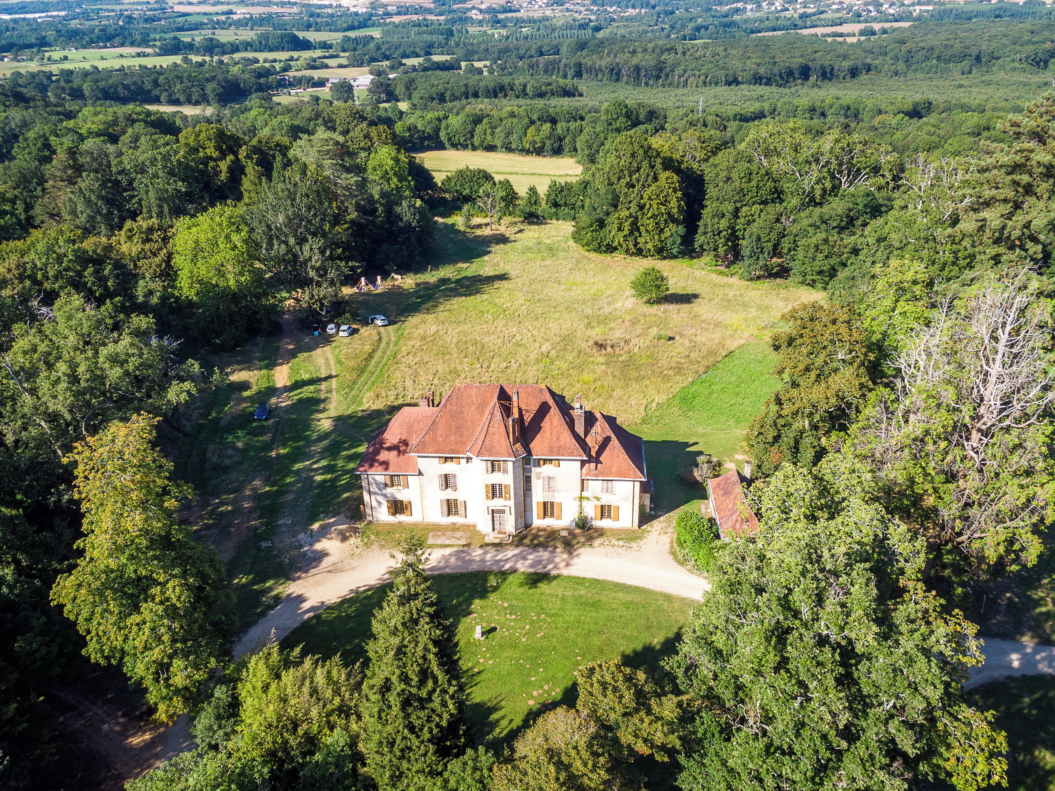 A large, two-story house with a red roof, surrounded by dense greenery and a well-maintained lawn.