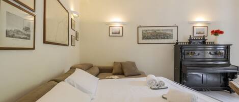 Una habitación de hotel con cama, sofá, piano y cuadros en la pared.