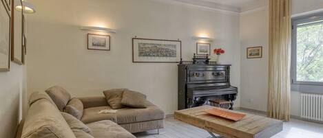 A living room with a sectional sofa, a piano, and framed artwork on the walls.