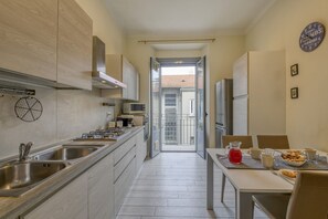 A modern kitchen with stainless steel appliances, a dining area with a table set for two, and a view through an open door to a balcony. - Tibaldi, 29 - Bright between Bocconi and Navigli (Milan)