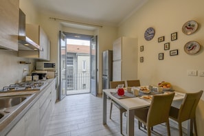 A modern kitchen with a gas stove, microwave, and refrigerator. There's a dining area with a table set for two, and a balcony with a view. - Tibaldi, 29 - Bright between Bocconi and Navigli (Milan)