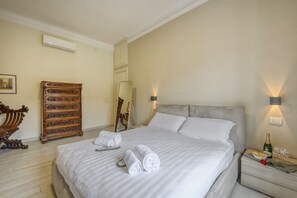 A neatly made bed with rolled towels, a wooden dresser, a bedside table with a bottle and glasses, and a wall-mounted lamp. - Tibaldi, 29 - Bright between Bocconi and Navigli (Milan)
