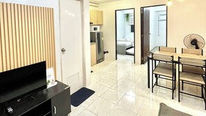 Ein modernes Wohnzimmer mit Flachbildfernseher, einem Essbereich mit Holztisch und Stühlen, einem Deckenventilator und einer Küche im Hintergrund.