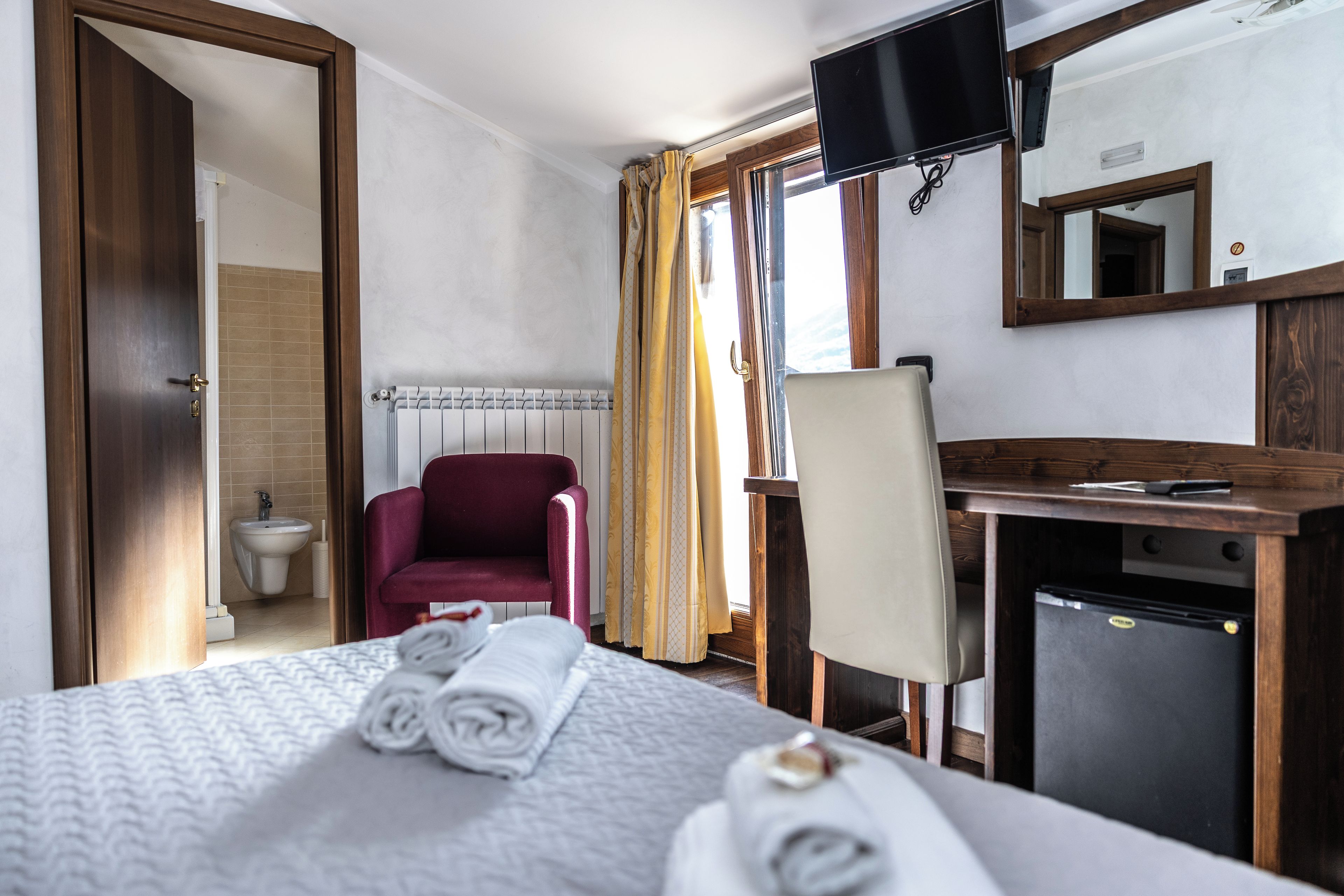 Une chambre d’hôtel équipée d’un lit, d’un bureau, d’une chaise, d’une télévision et d’un petit réfrigérateur.