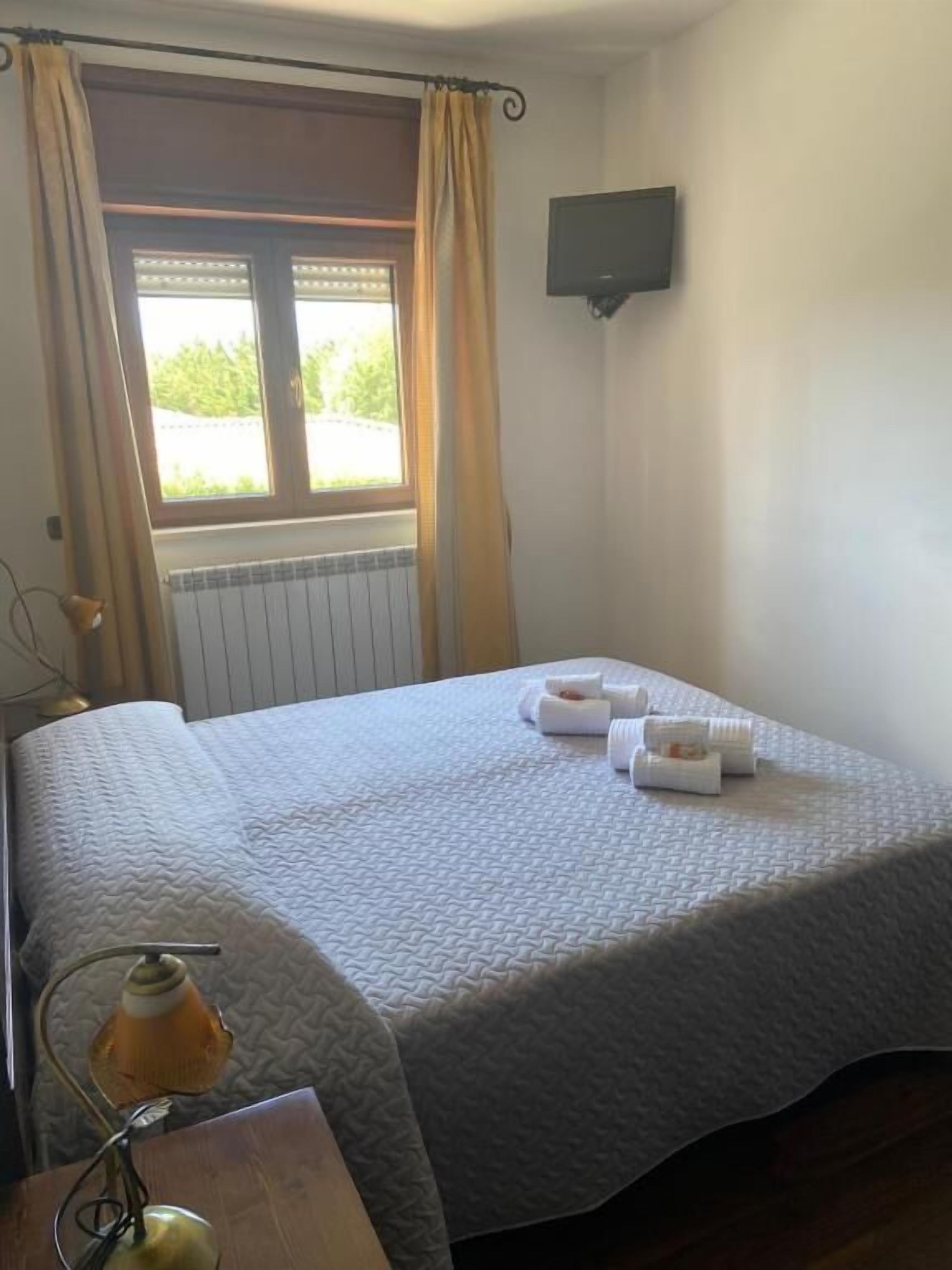 A single bed with a quilted bedspread, a bedside table with a lamp, and a window with curtains.