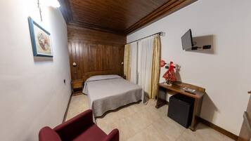 Un dormitorio con cama, escritorio, silla, televisor y un refrigerador pequeño.