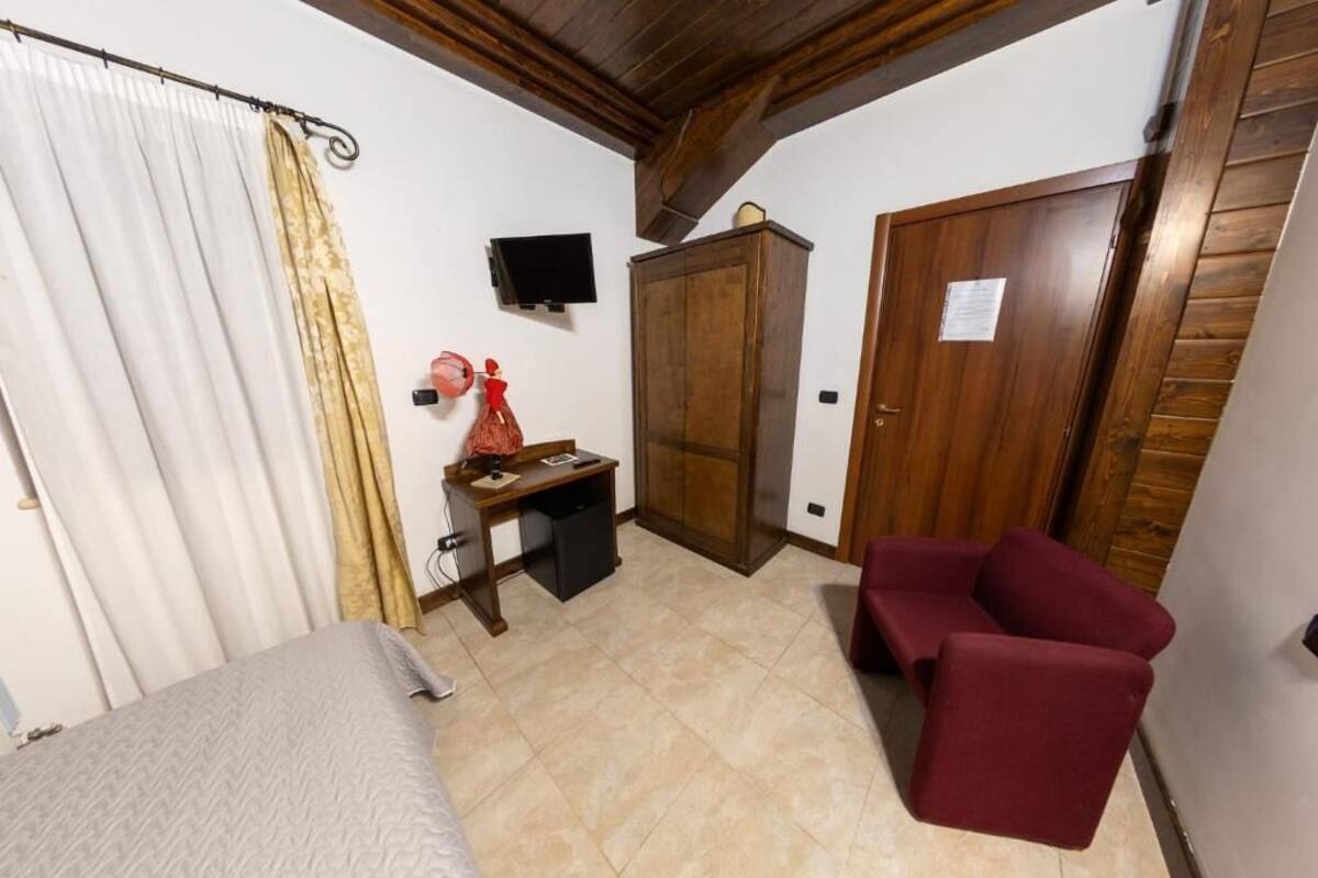 A room with a bed, a desk with a chair, a wardrobe, a television, and a red armchair.